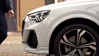 Side view of Audi Q3 bonnet and wheel and mans hand infront.