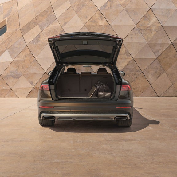 Audi Q8 tfsi e facing modern wall with boot open.