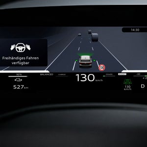 Nahaufnahme eines Displays im Fahrzeuginnenraum. Abgebildet ist die Silhouette eine Fahrzeugs in Geradeausfahrt. Links daneben ein Textkasten, der Informationen über das assistierte freihändige Fahren gibt.
