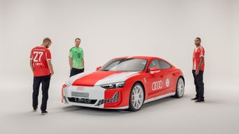 Drei Fußballspieler vom FC Bayern München stehen um einen rot-weißen RS e-tron GT herum