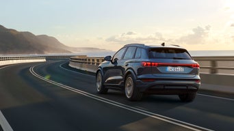 Ein blauer Audi Q6 SUV e-tron auf der Straße in ländlichem Setting und Gegenlicht.