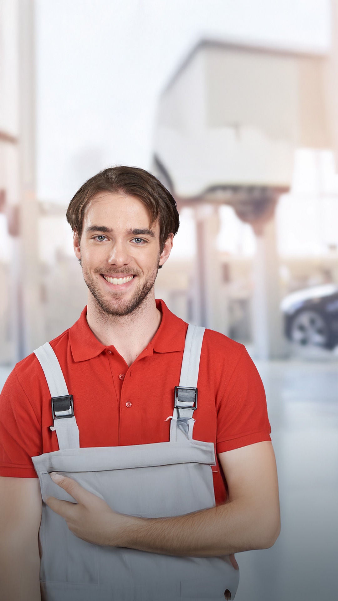 Mitarbeiter in Arbeitskleidung lächelt in die Kamera. Im Hintergrund ist eine Werkstatt zu sehen.