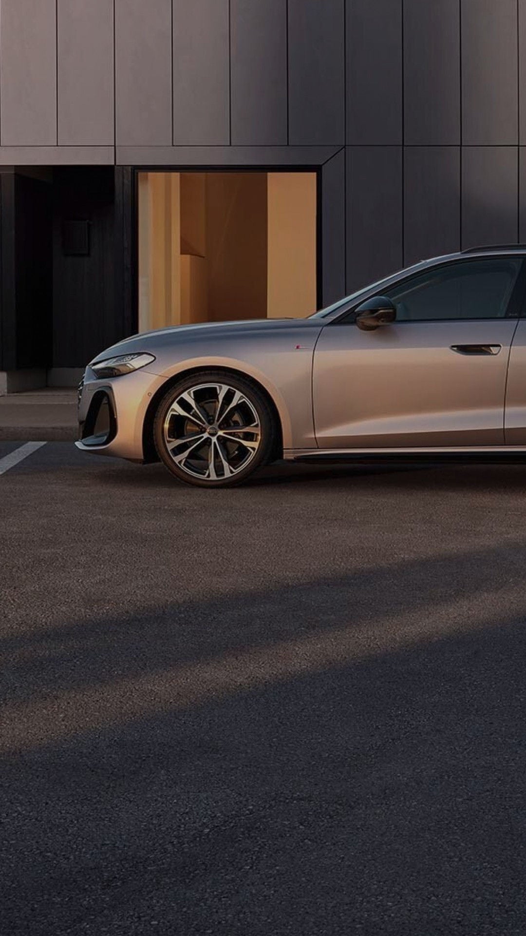 A silver Audi A5 Avant parked beside a modern building, showcasing its stylish design and sporty wheels in soft evening light.