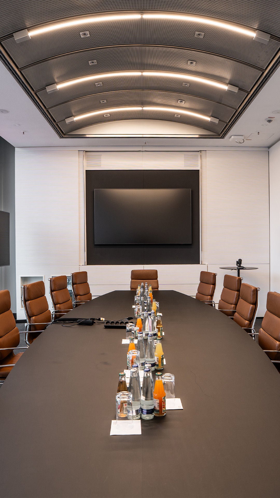 Moderner Konferenzraum mit langem Tisch, braunen Ledersesseln und Getränken auf dem Tisch.