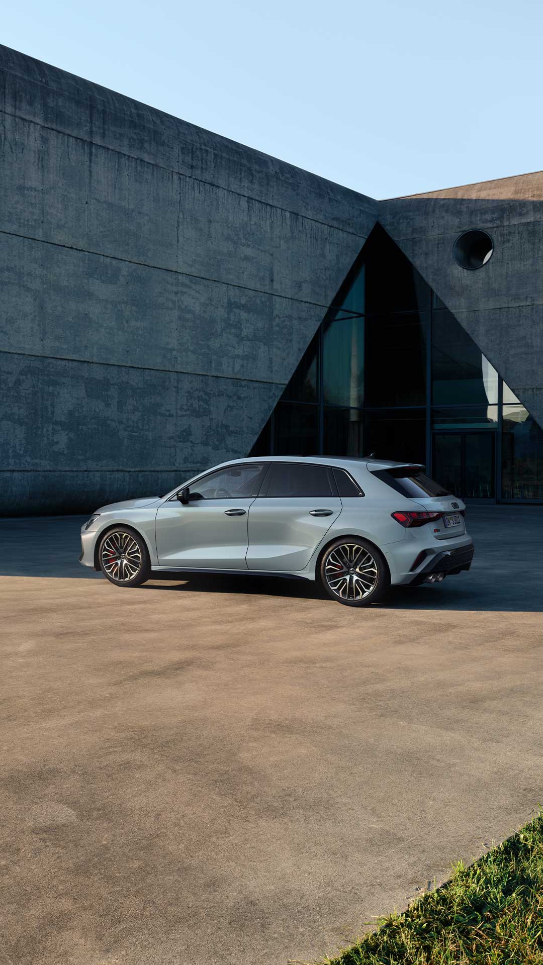Seitenansicht eines silbernen Audi S3 Sportback mit roten Bremssätteln vor moderner Gebäudefassade.