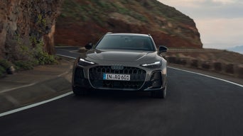 De Audi A6 allroad wordt van voren gezien terwijl hij langs een kronkelende bergweg rijdt. Links verrijzen steile rotswanden.