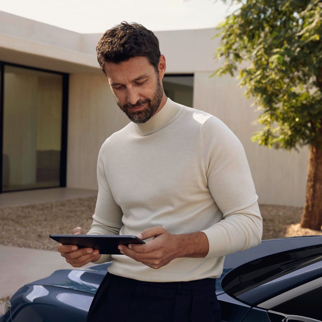 A man leaning on a car holding a tablet