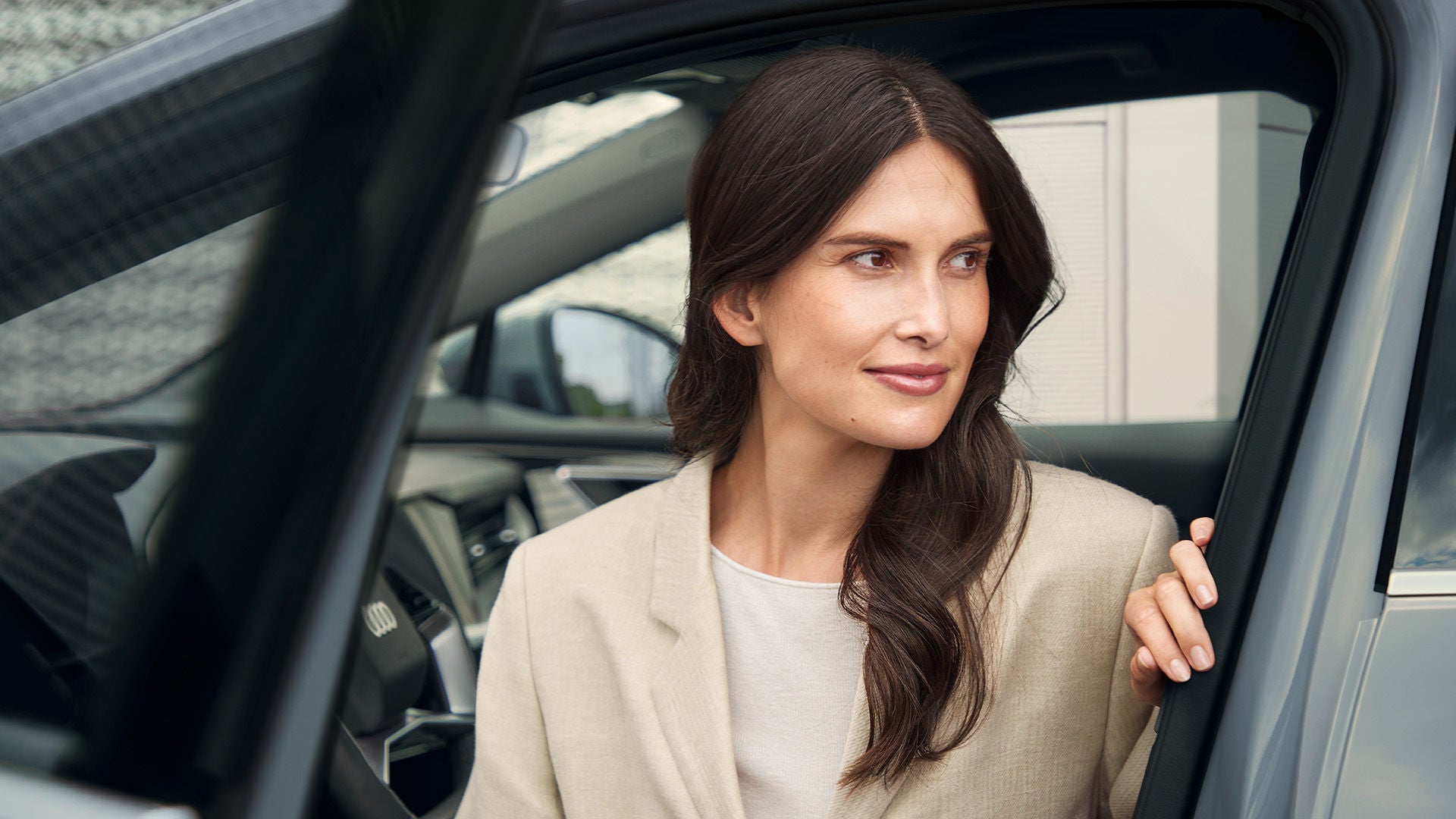 Frau mit dunklen Haaren steigt aus einem Audi und blickt zur Seite, helle moderne Umgebung.