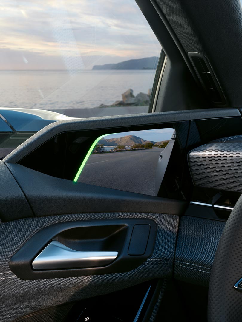 Digitale Außenspiegelanzeige im Audi A6 Avant e-tron zeigt Straßenansicht mit Bergkulisse.
