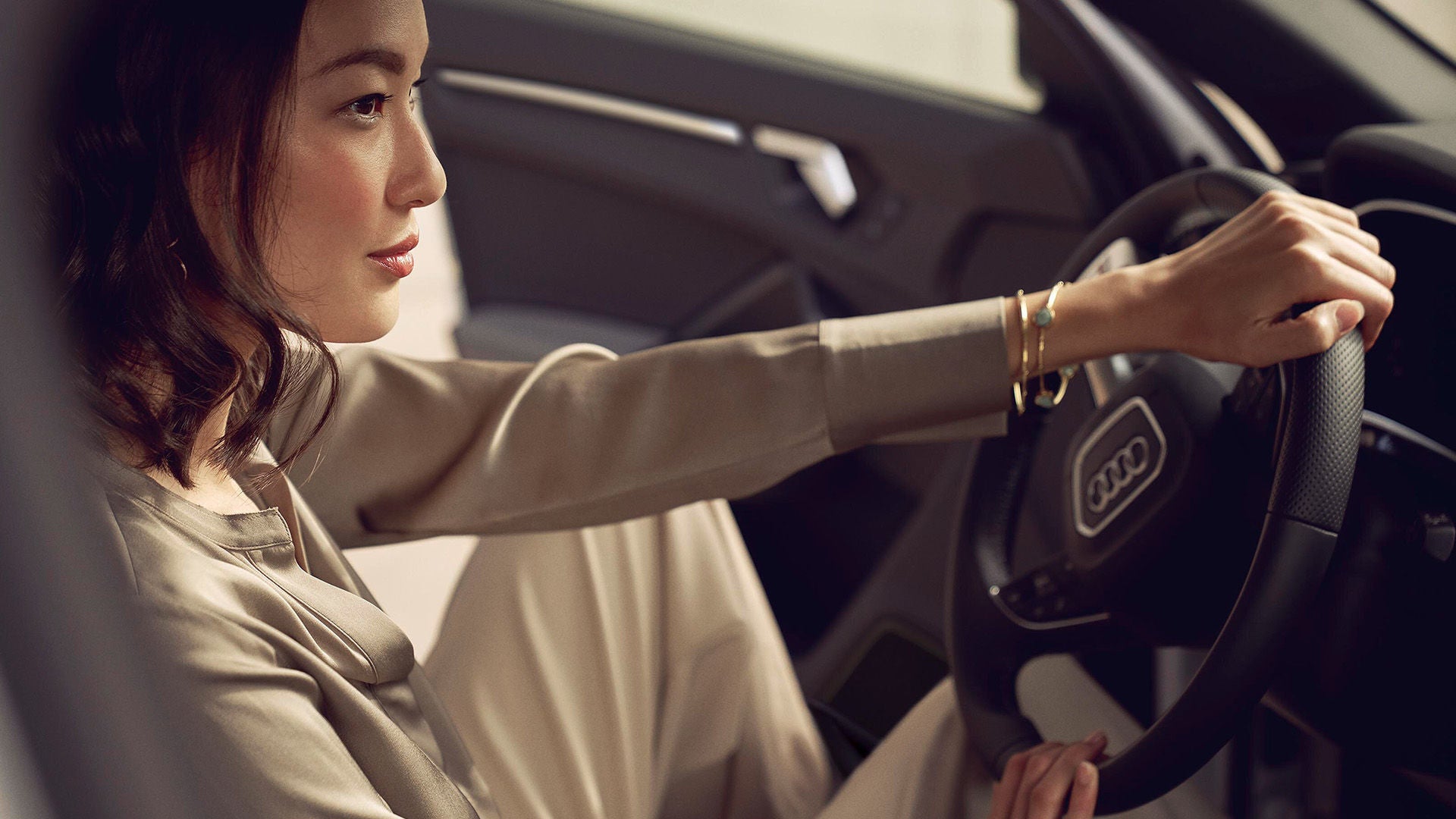 Frau am Steuer eines Audi, sitzt konzentriert im Fahrzeuginterieur und blickt nach vorn – Nahaufnahme von der Seite.