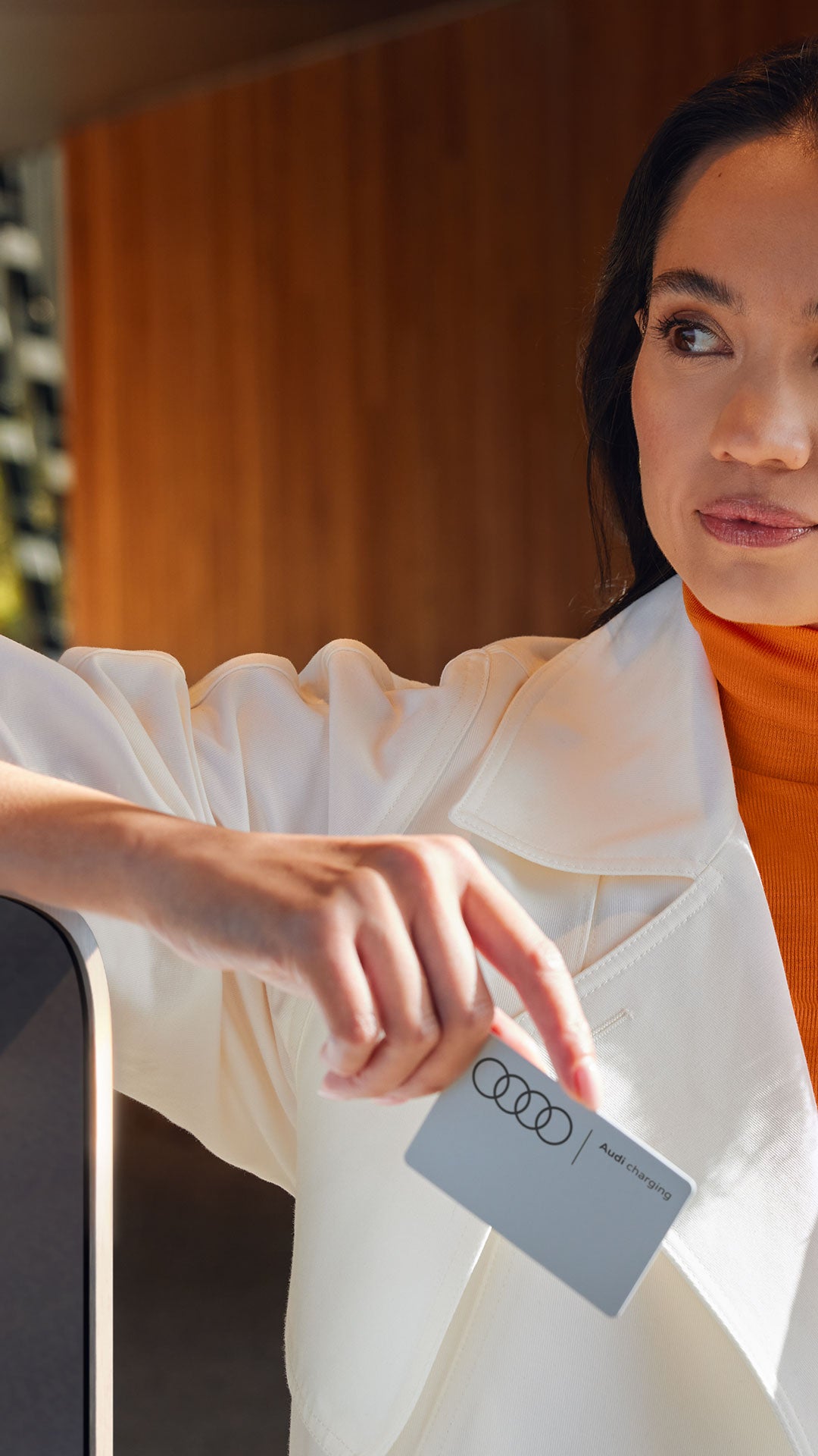 Eine Frau lehnt an einer Ladesäule mit einer Ladekarte in der Hand