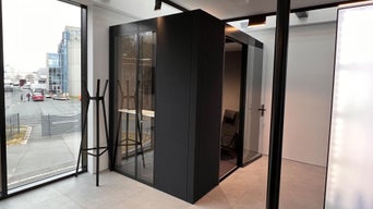 Kleine schwarze Meetingbox mit Glastüren steht in modernem Raum mit großen Fenstern und Blick nach draußen.