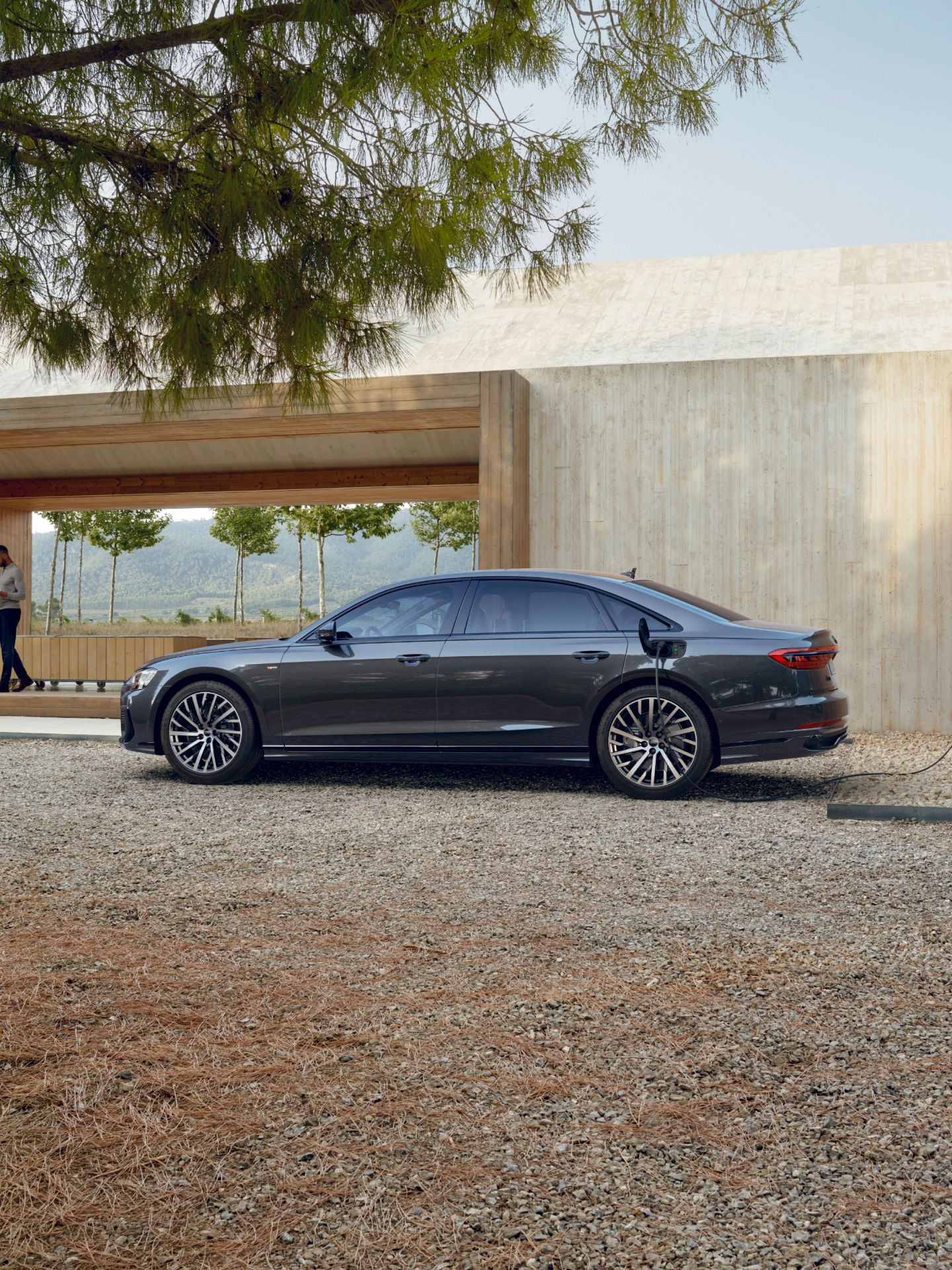 A black sedan charging at an outdoor station, with a modern wooden building in the background.