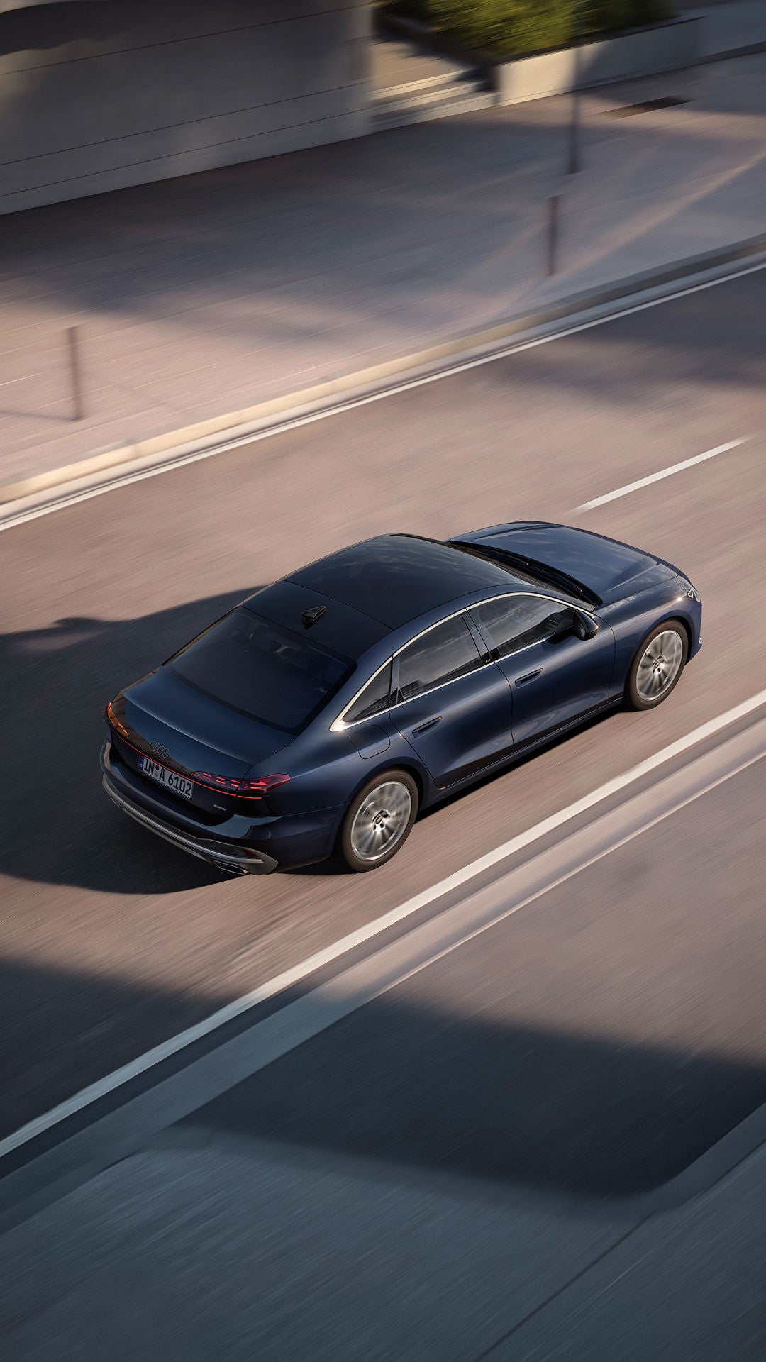 A dark blue Audi luxury sedan cruising on a smooth road, showcasing its sleek design and modern features from an aerial view.