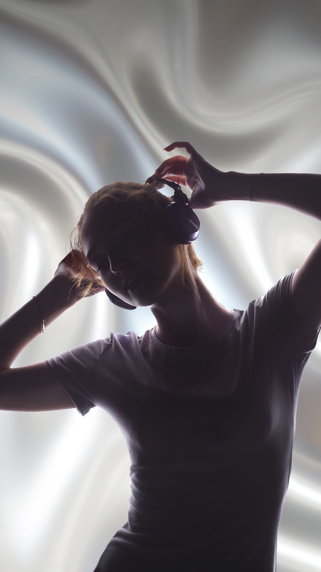 Silhouette einer Frau mit Kopfhörern, Arme über dem Kopf, vor hellem, wirbelndem Licht-Hintergrund.