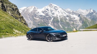 Dunkelgrauer Audi RS e-tron GT performance steht auf einem Parkplatz vor schneebedeckten Bergen bei Sonnenschein.
