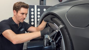 Audi-Mitarbeiter justiert ein Messgerät am Vorderrad eines Fahrzeugs in einer Werkstattumgebung.