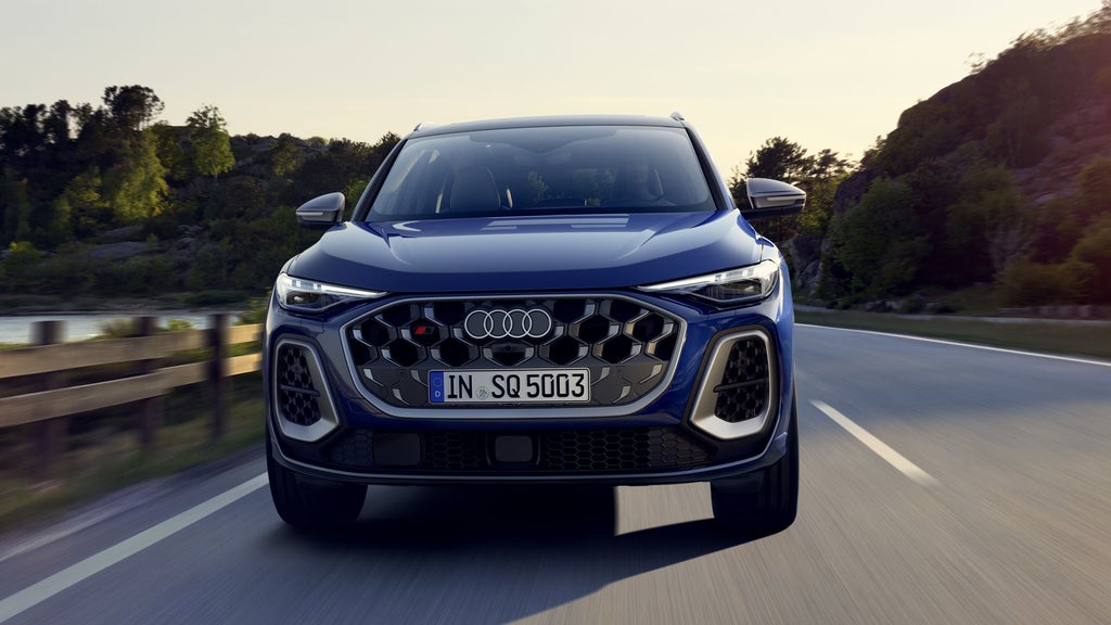 Frontprofil des SQ5 SUV in dunkelblau, welcher auf einer Straße durch die Natur fährt. Am Steuer sitzt eine junge Frau.&nbsp;