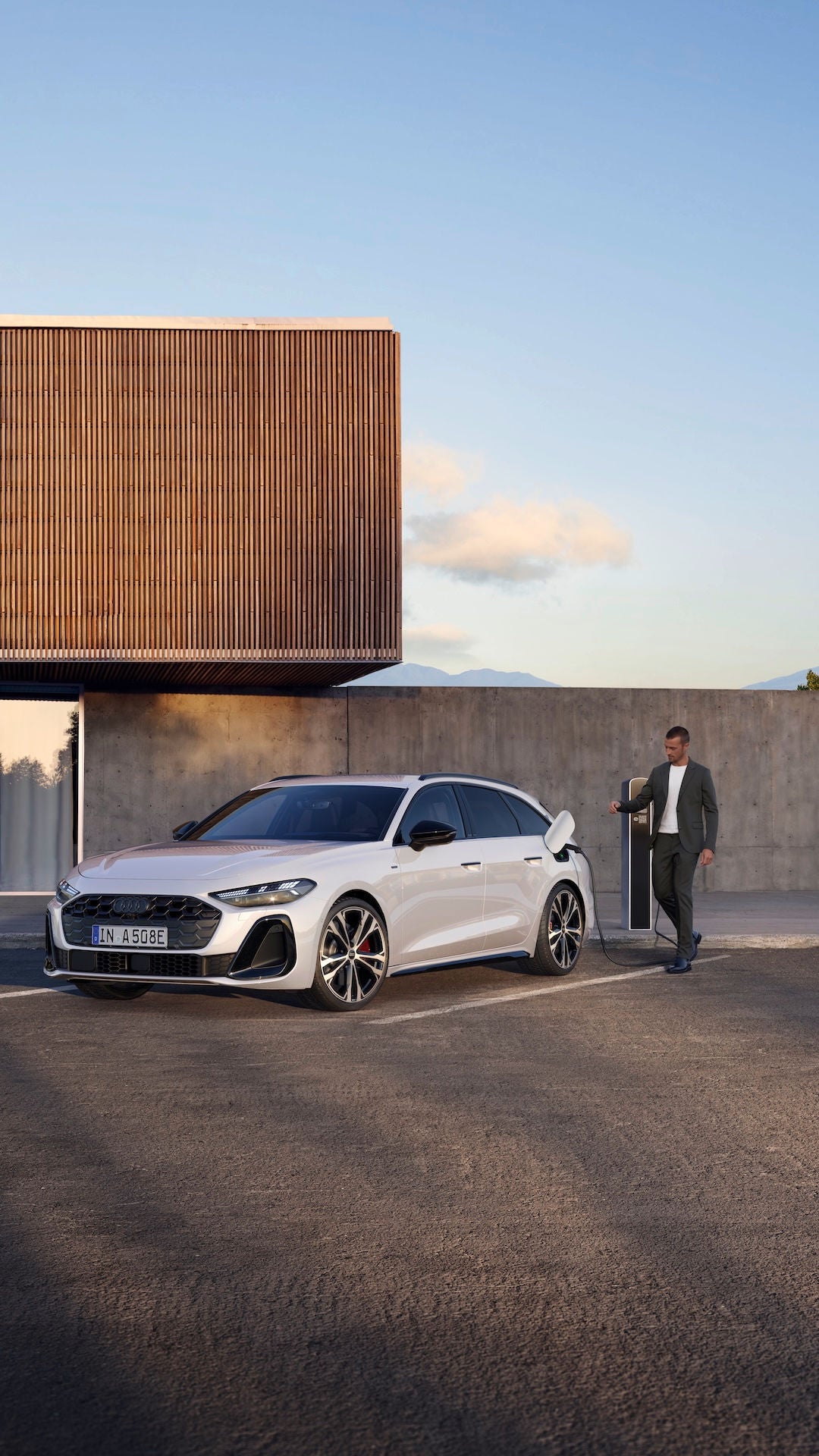 Audi A5 Avant e-hybrid parcheggiata e in ricarica elettrica, un uomo si avvicina per staccare la presa di collegamento