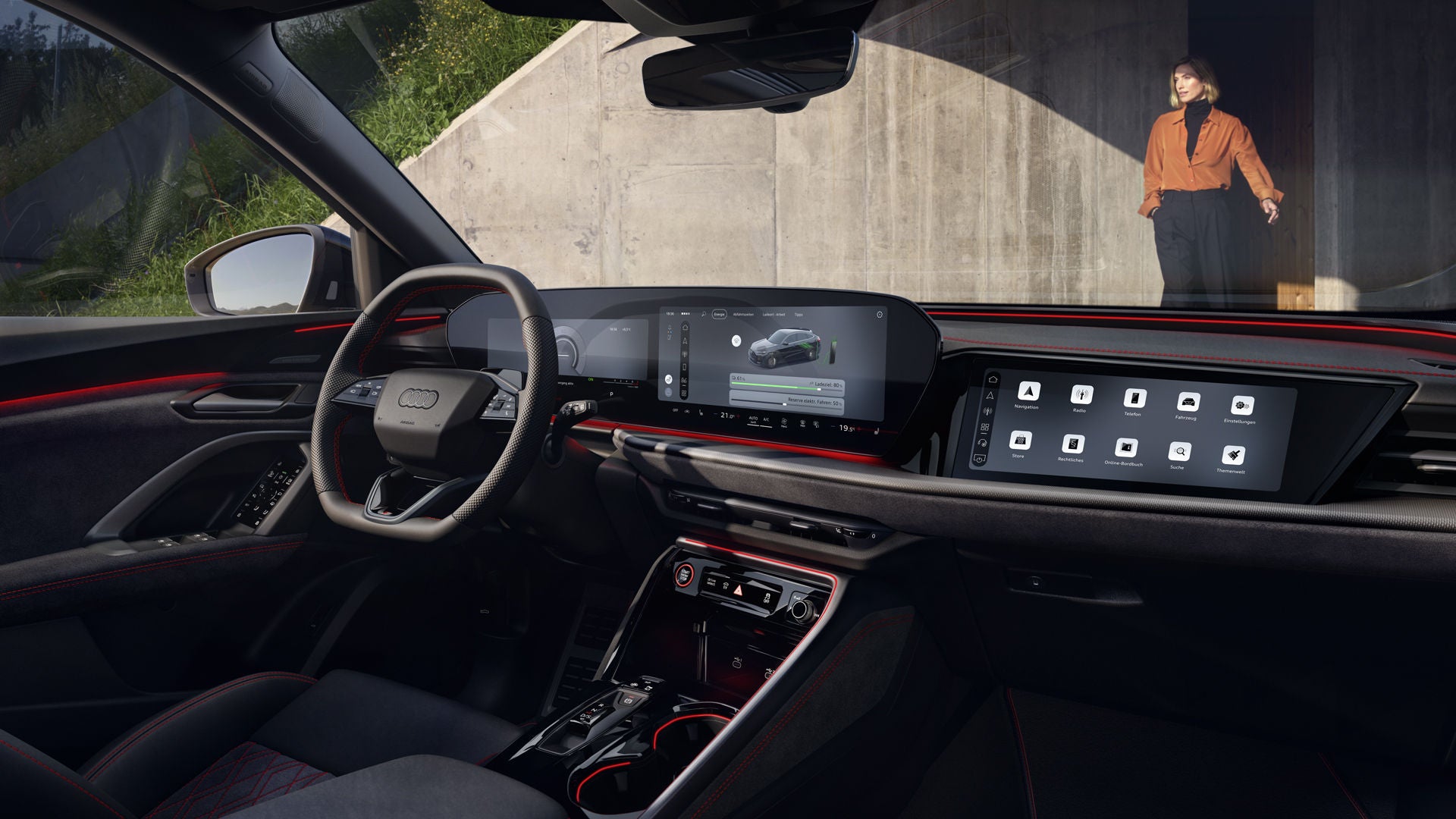 Der Innenraum des Q5 Sportback e-hybrid mit Fokus auf das Lenkrad und die digitalen Displays. Vor dem Fahrzeug steht eine modisch gekleidete, junge Frau.