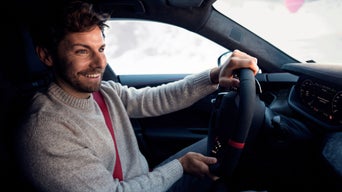 A smiling man behind the wheel of an Audi; the interior is dark gray; snow can be seen through the windshield.