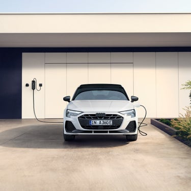 Weißer Audi A3 Sportback TFSI e von vorn an einer Ladestation vor moderner Garage mit klaren Linien.