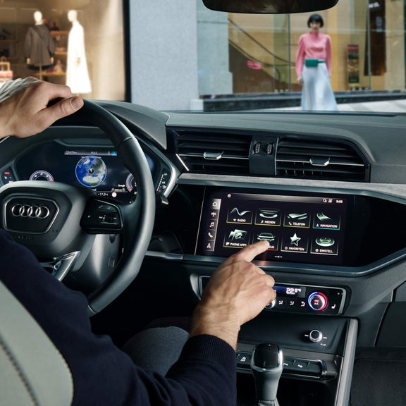 Inside view of driver using Audi Q3 touchscreen panel whilst holding the steering wheel.