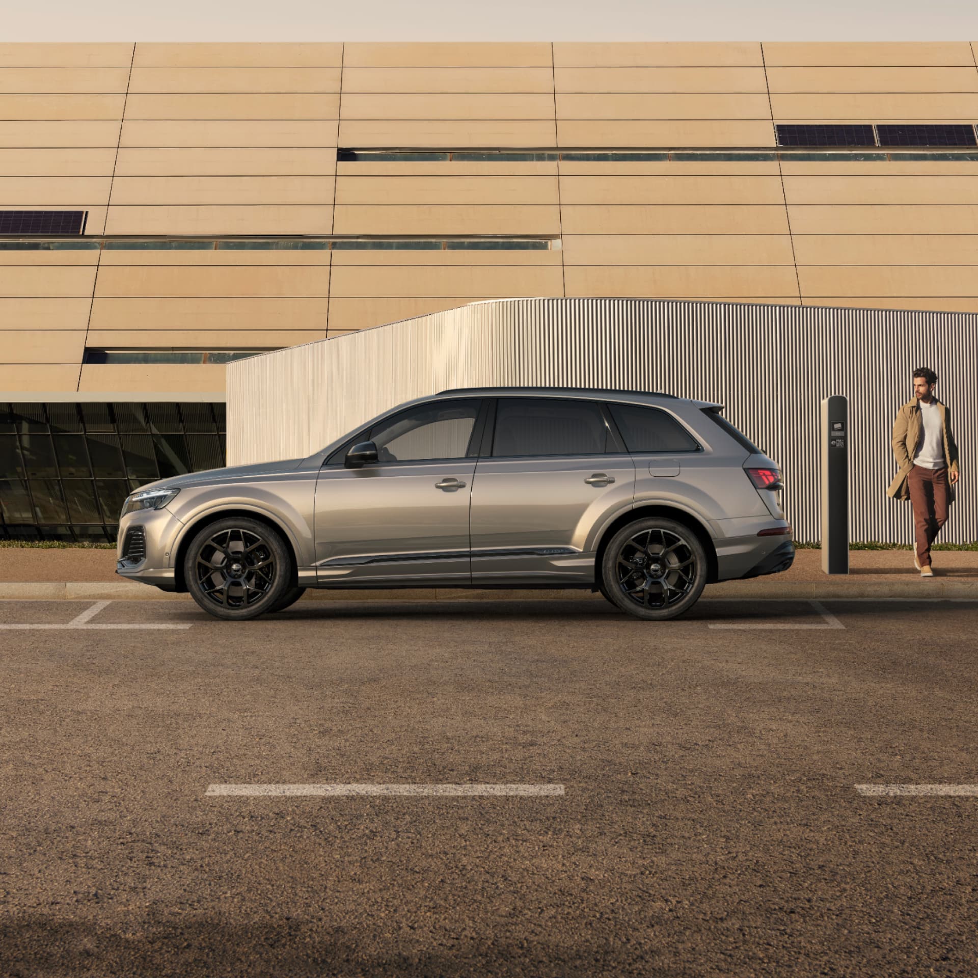 A silver SUV parked beside a charging station with a modern building in the background.