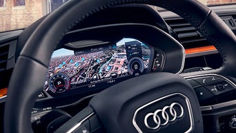 3D-Stadtkarte auf dem digitalen Tacho hinter dem Audi-Lenkrad mit eingeblendeter Navigation.