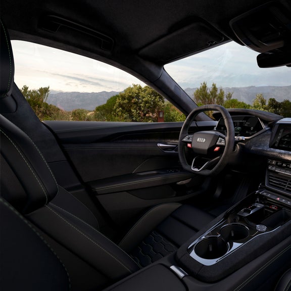 Innenraum eines Audi RS e-tron GT performance mit schwarzem Leder, Lenkrad, Touchscreen und Blick auf grüne Landschaft mit Bergen.
