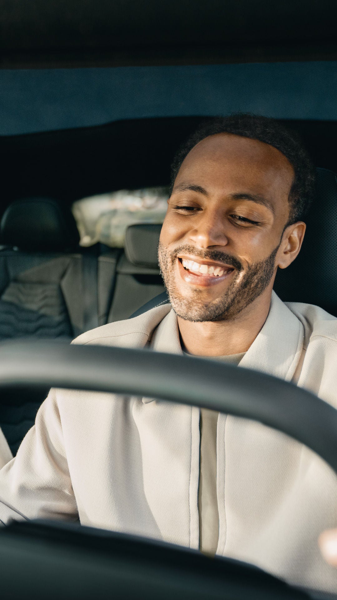 Ein Mann und eine Frau sitzen gemeinsam lächelnd in einem Auto. Die Perspektive ist von vorne durch die Windschutzscheibe aufgenommen.