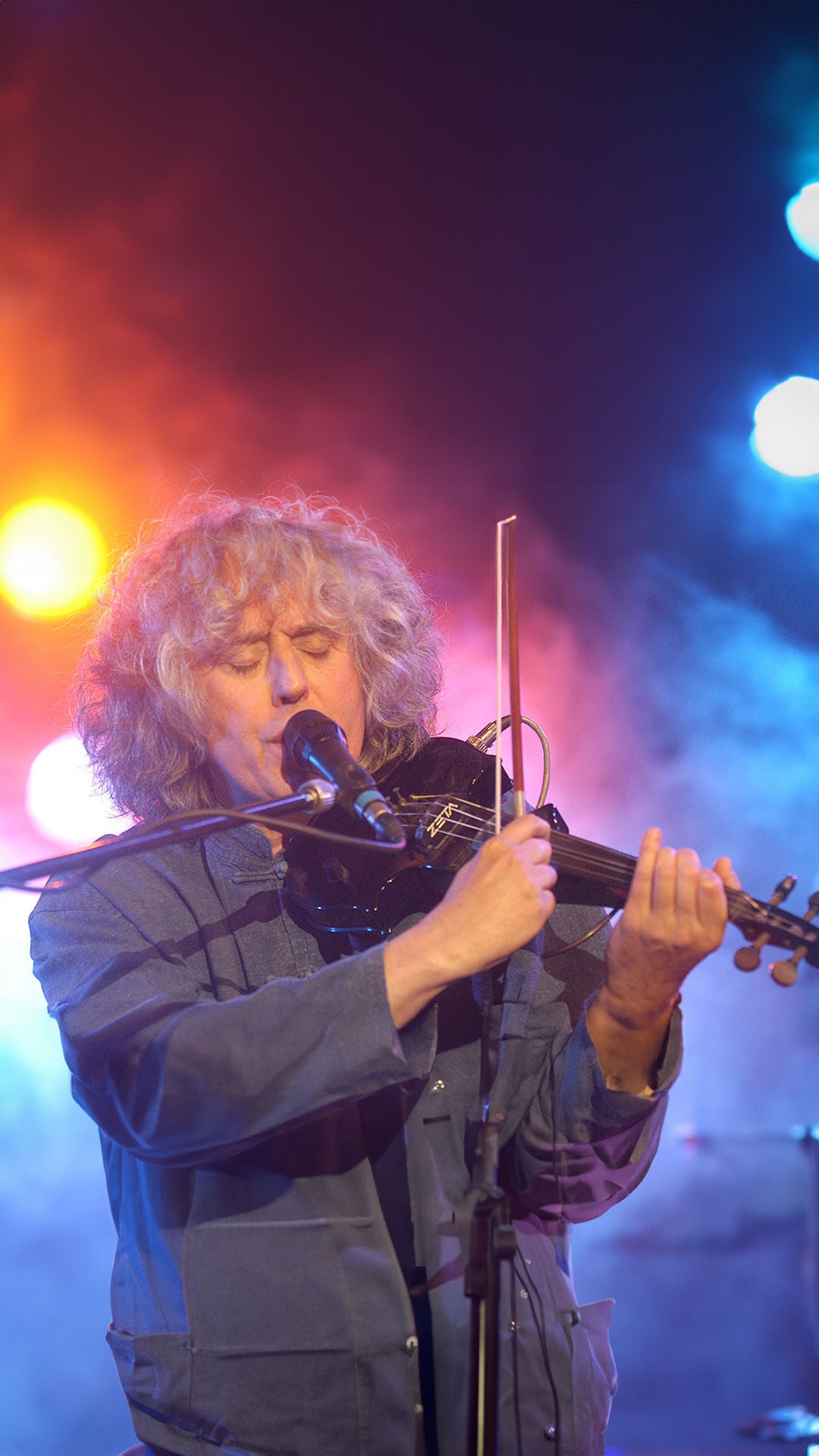 Mann mit lockigen grauen Haaren spielt E-Violine auf der Bühne.