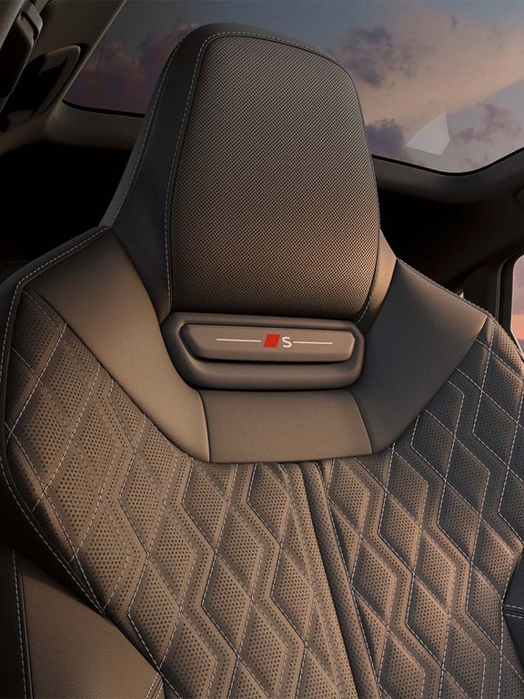 Nahaufnahme einer schwarzen Sportsitzlehne mit S-Logo und Kontrastnähten bei Sonnenuntergang.