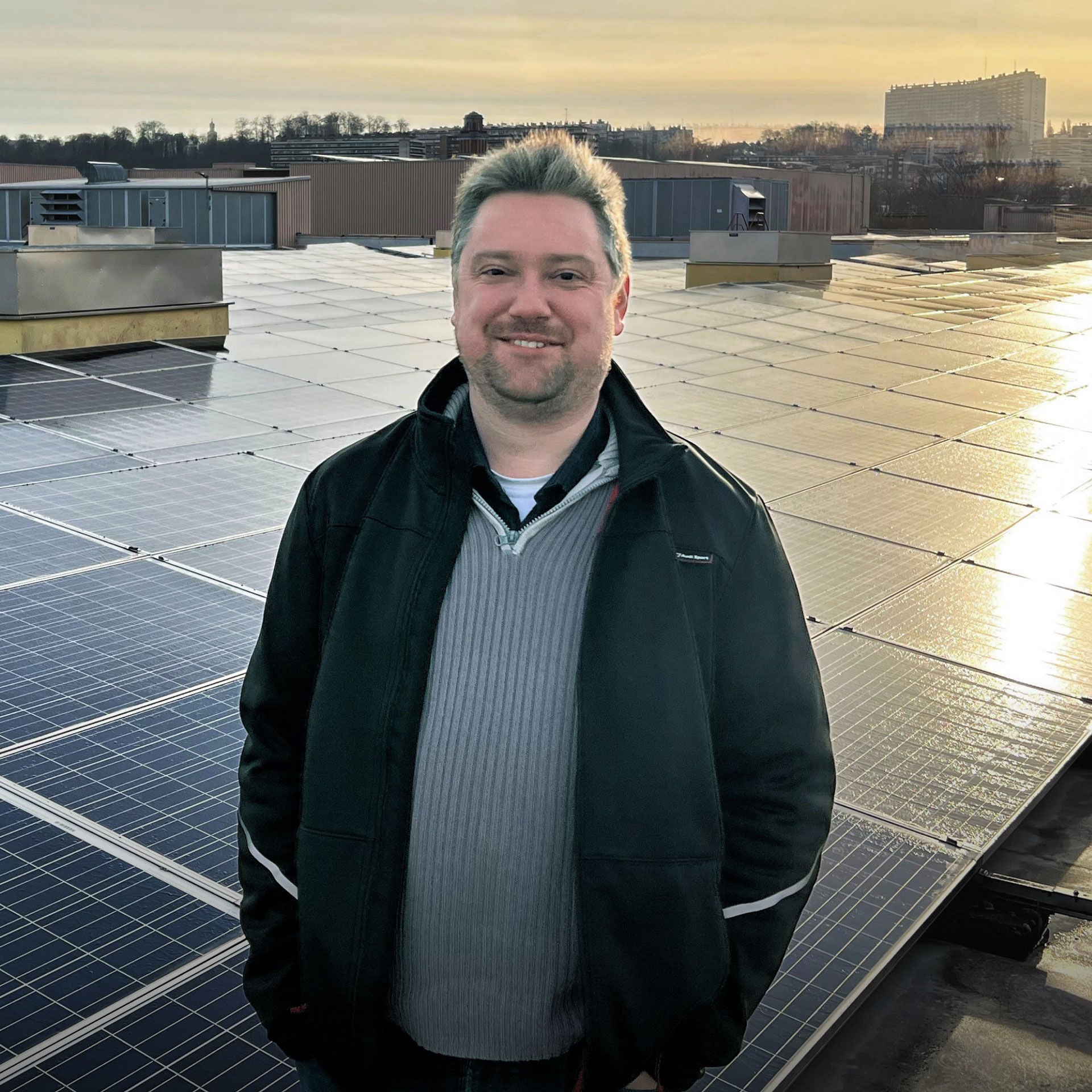 Christian Stragier, Umweltkoordinator bei Audi Brüssel, steht bei Sonnenuntergang vor einer großen Fläche mit Solarpaneelen auf einem Dach. 