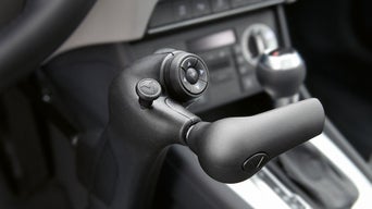 Detailansicht einer Handbedienhilfe im Auto für Menschen mit körperlicher Behinderung, montiert neben dem Lenkrad.