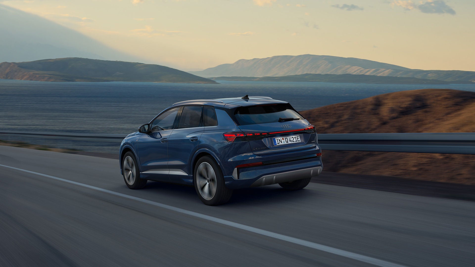 Une Audi Q4 e-tron bleue sur une route dans un paysage montagneux.