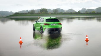 Light green Audi RS 3 Sportback drives over a large puddle on a training ground.