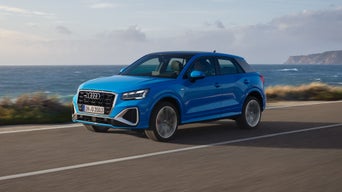 Ein blauer Audi fährt auf einer Straße direkt am Wasser vor einer Küstenlandschaft.