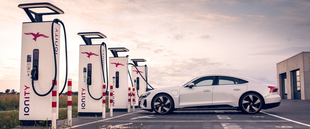 Ein weißer Audi e-tron GT quattro steht an einer Ladesäule vor einem Sonnenuntergang