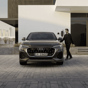Man in black outfit charging Audi Q8 tfsi e outside contemporary home.