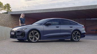 Der A6 Sportback e-tron steht im Seitenprofil vor dem Carport eines Hauses. Daneben steht eine junge Frau.