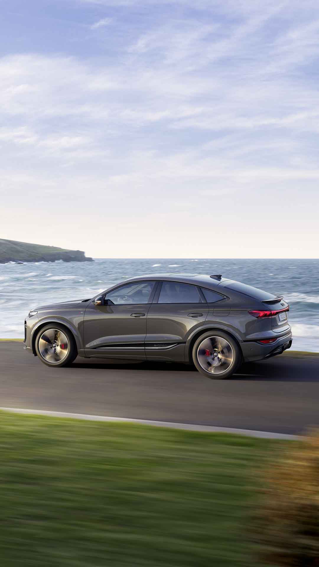 Side view of the Q6 Sportback e-tron driving along a road by the sea.
