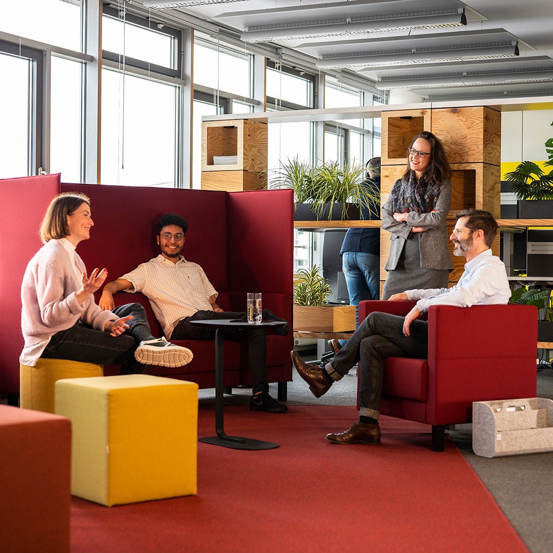 In einem modernen Büro unterhalten sich drei Personen, während eine vierte steht