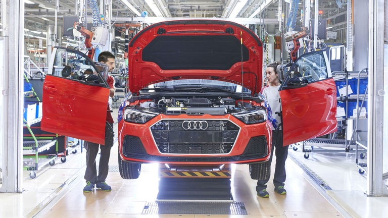 Zwei Mitarbeitende montieren ein rotes Audi-Fahrzeug in einer Produktionshalle.