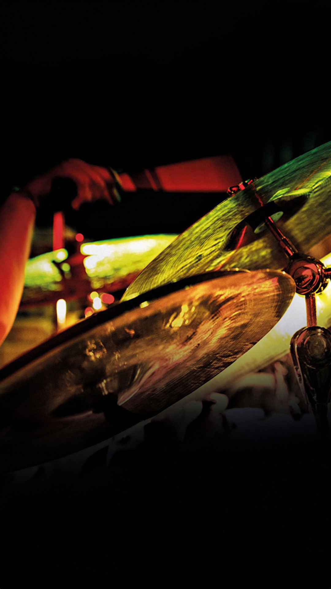 Nahaufnahme eines Schlagzeugers, der bei dunkler Bühnenbeleuchtung ein leuchtend grünes Becken anschlägt.