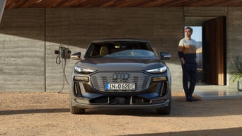 Auto zu Hause an einer Ladestation mit einem Mann, der rechts am Auto vorbei geht