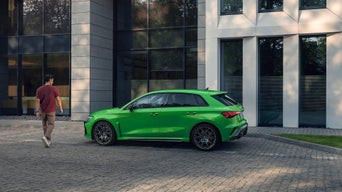 Ein grüner Audi steht vor einem modernen Bürogebäude, ein Mann geht vom Fahrzeug weg.