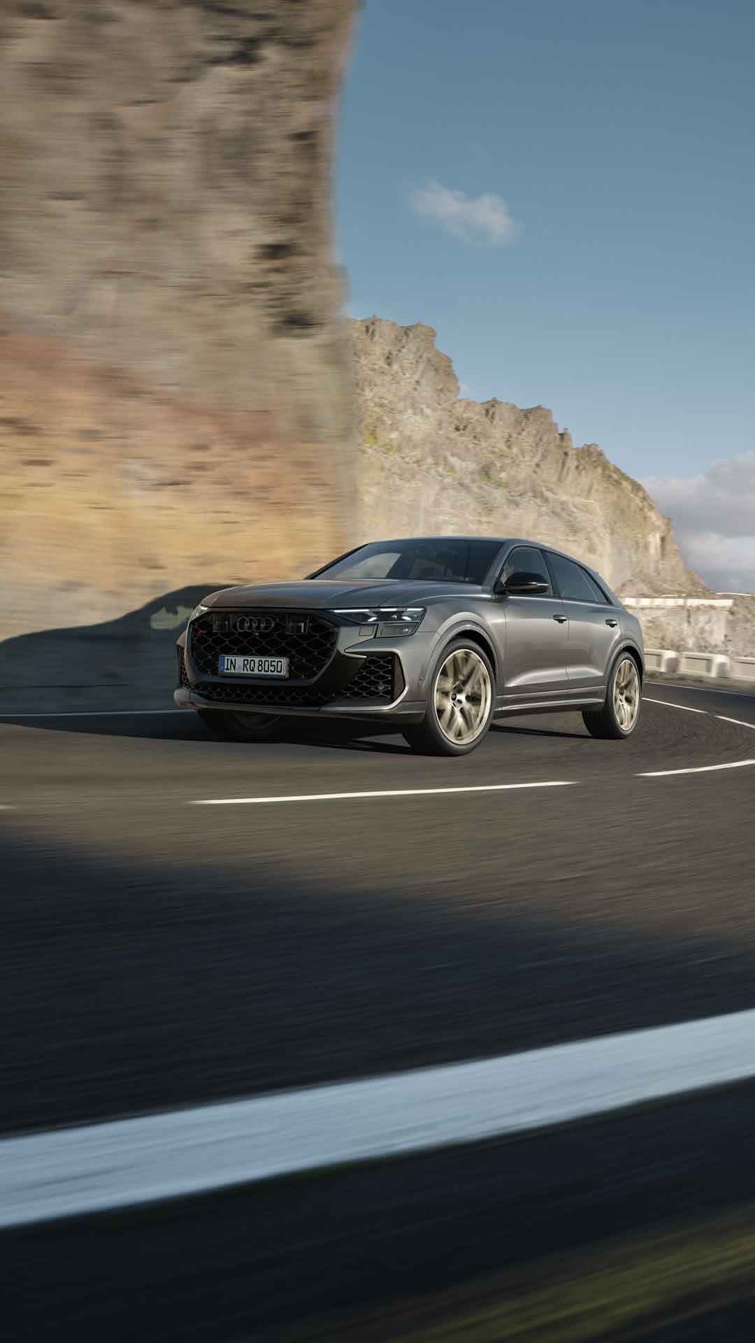 Ein grauer Audi RS Q8 SUV fährt auf kurviger Straße vor Felswand.