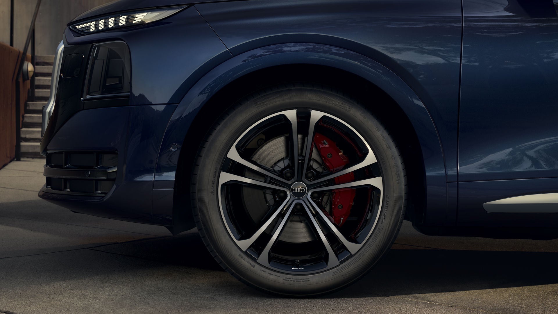 Gros plan sur la roue avant gauche, équipée de jantes en alliage Audi Sport de 22 pouces au design à 5 doubles branches, de couleur noir métallisé et dotées d'une finition polie.