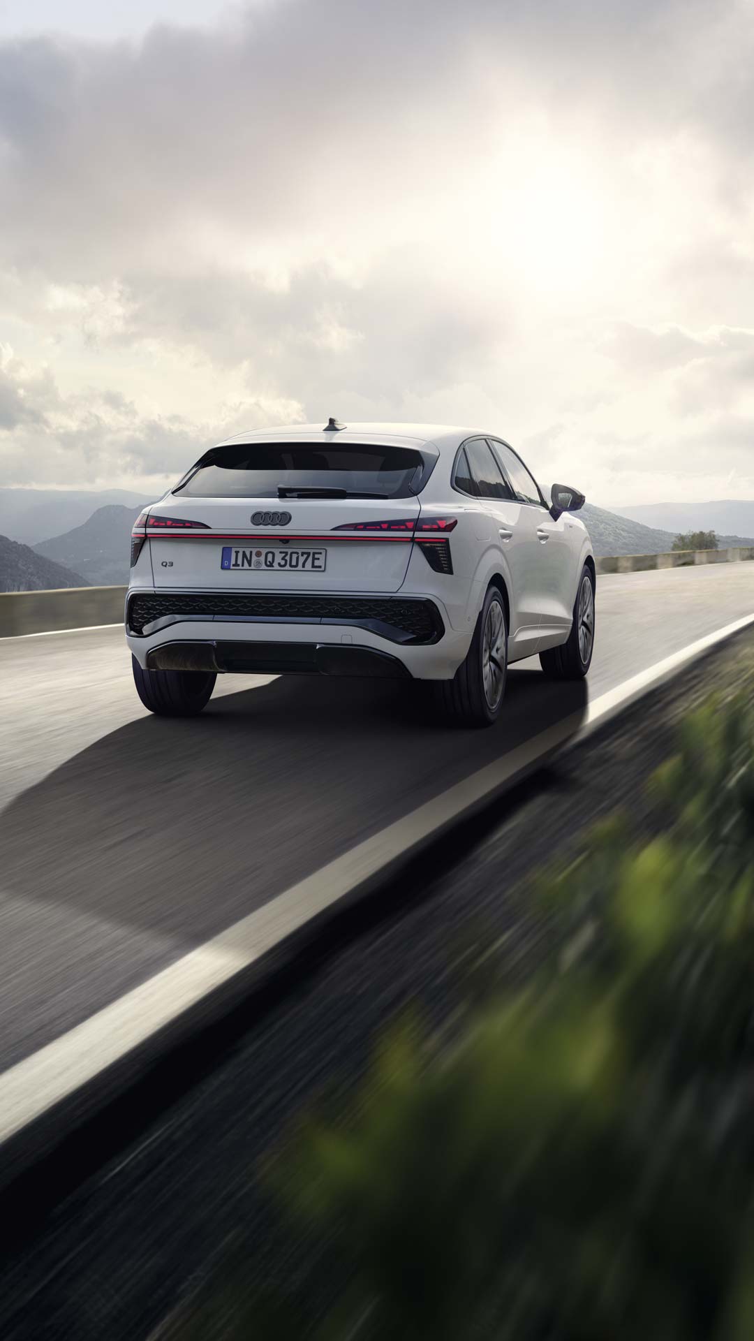 A white Q3 Sportback e-hybrid drives along a country road in a mountainous landscape.	